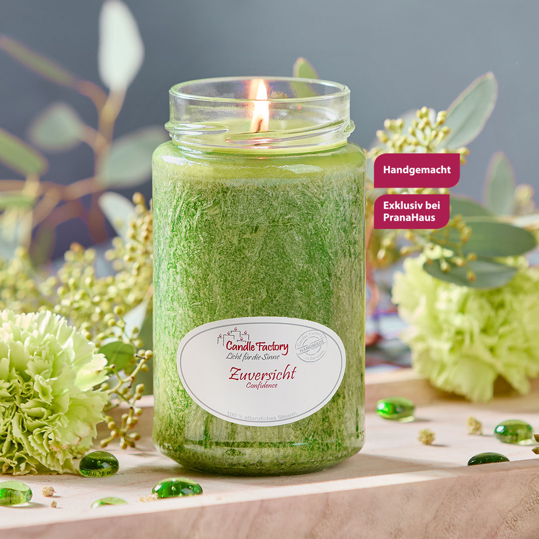 Eine hellgrüne Duftkerze im Glas, auf dem Etikett steht der Name "Zuversicht". Zwei Labels weisen die Kerze als exklusiv und handgemacht aus.