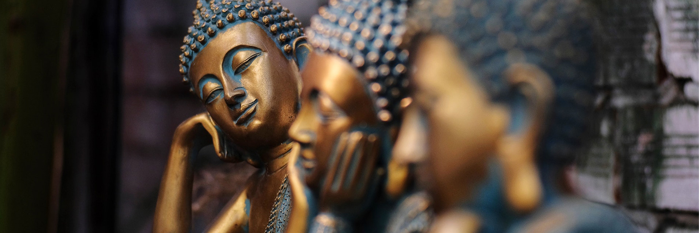 Drei goldene Buddha-Statuen in jeweils unterschiedlicher Haltung. Die vordere ist nur unscharf zu erkennen, die zweite hat den Kopf in die Hände gestützt, die dritte neigt den Kopf zur Seite.