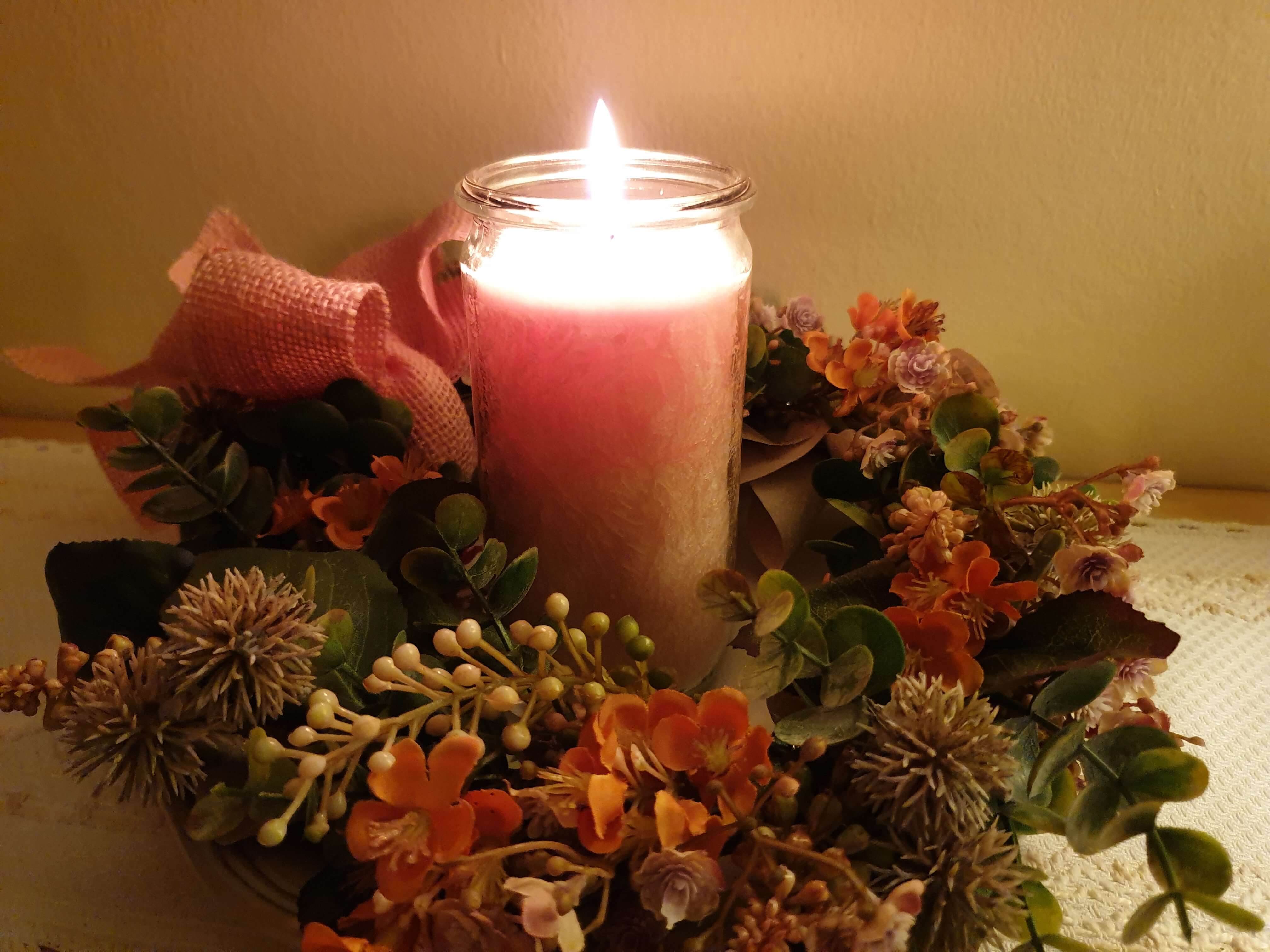 Brennende Kerze in einem Blumenkranz mit Schleife