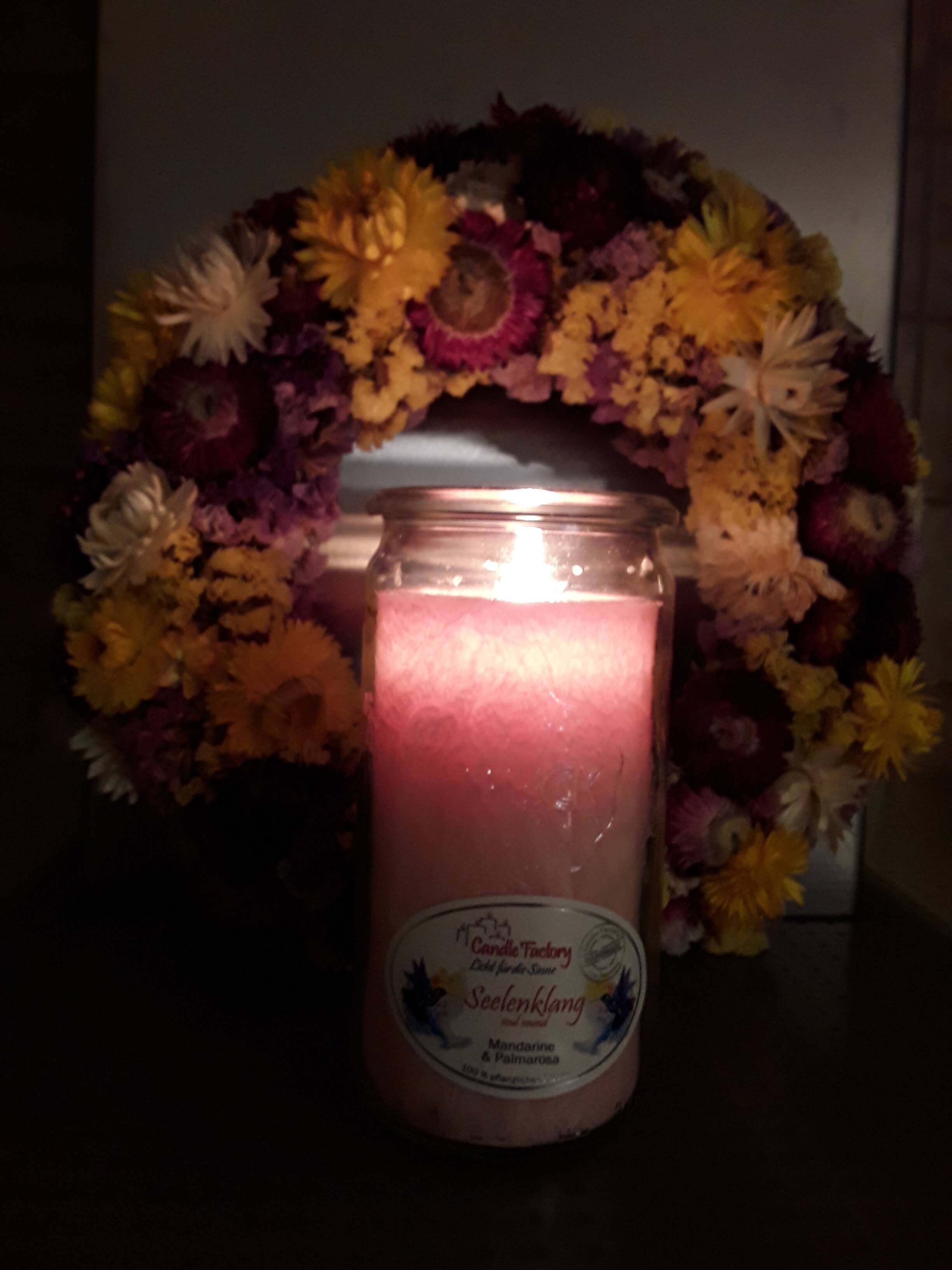 Brennende Kerze vor einem Blumenkranz, der aufrecht an der Wand lehnt