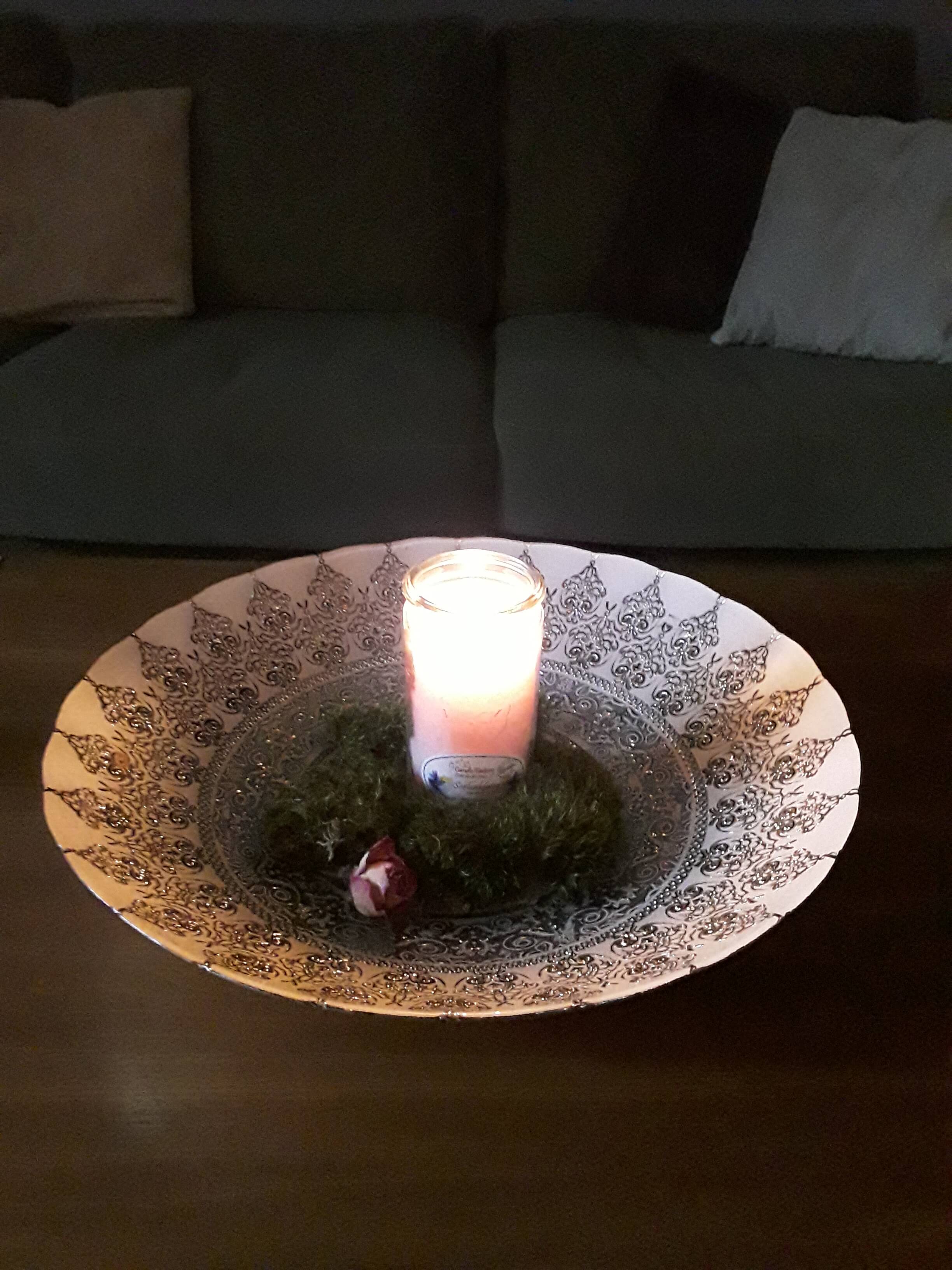 Brennende Kerze in einem großen, mit Ornamenten verzierten Teller