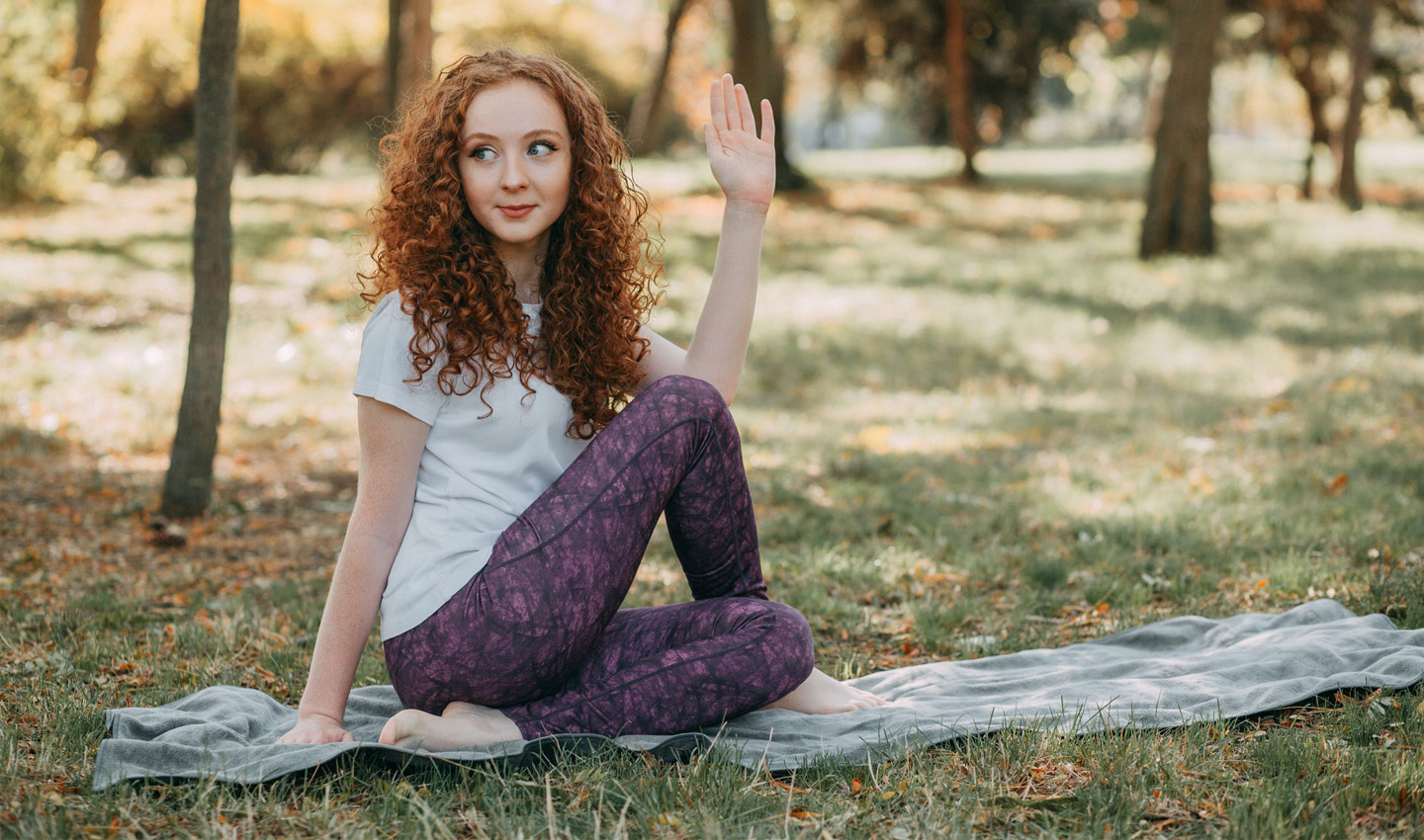 Junge Frau übt die Yoga-Pose "Drehsitz" in einem Park