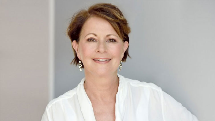 Porträt von Stefanie Stahl. Sie trägt eine weiße Bluse und passende Ohrringe und lächelt in die Kamera