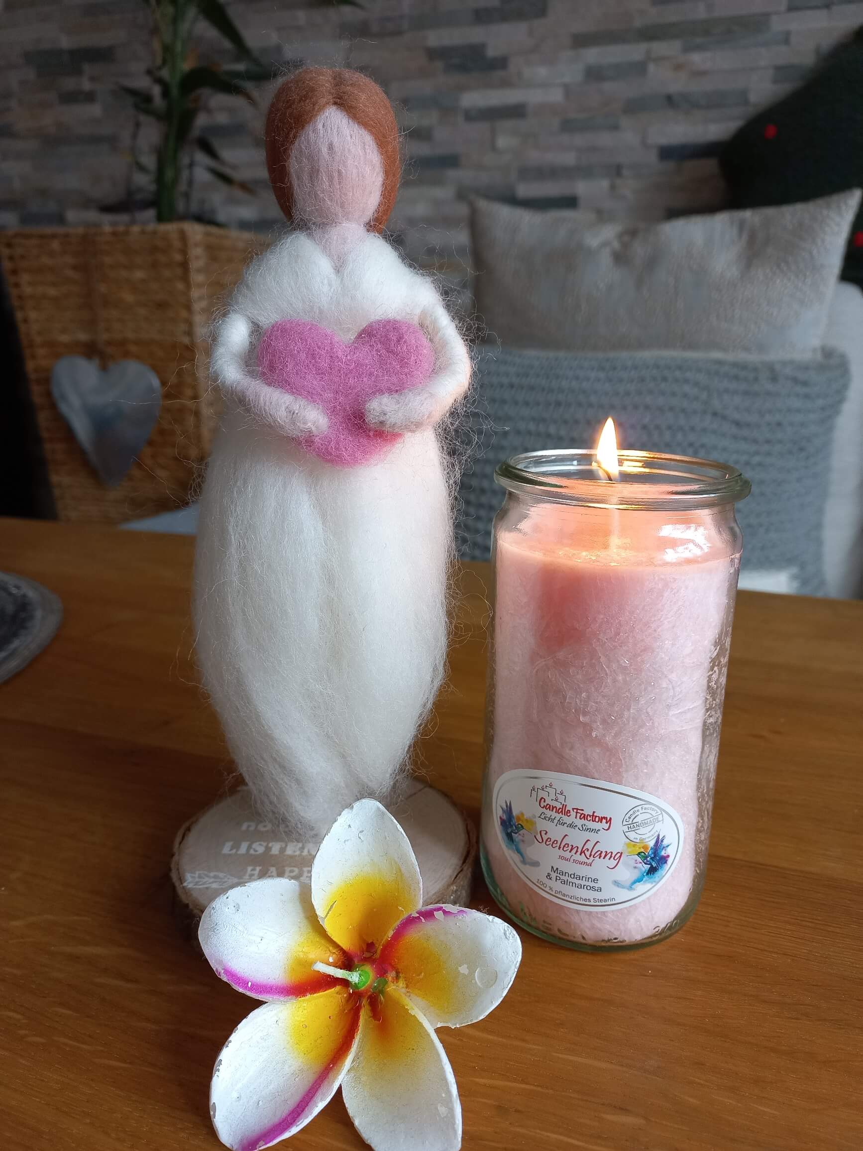 Brennende Kerze neben einer gefilzten Engelsfigur und einer exotischen Blüte