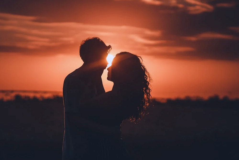 Silhouette eines sich umarmenden Paares vor der untergehenden Sonne.
