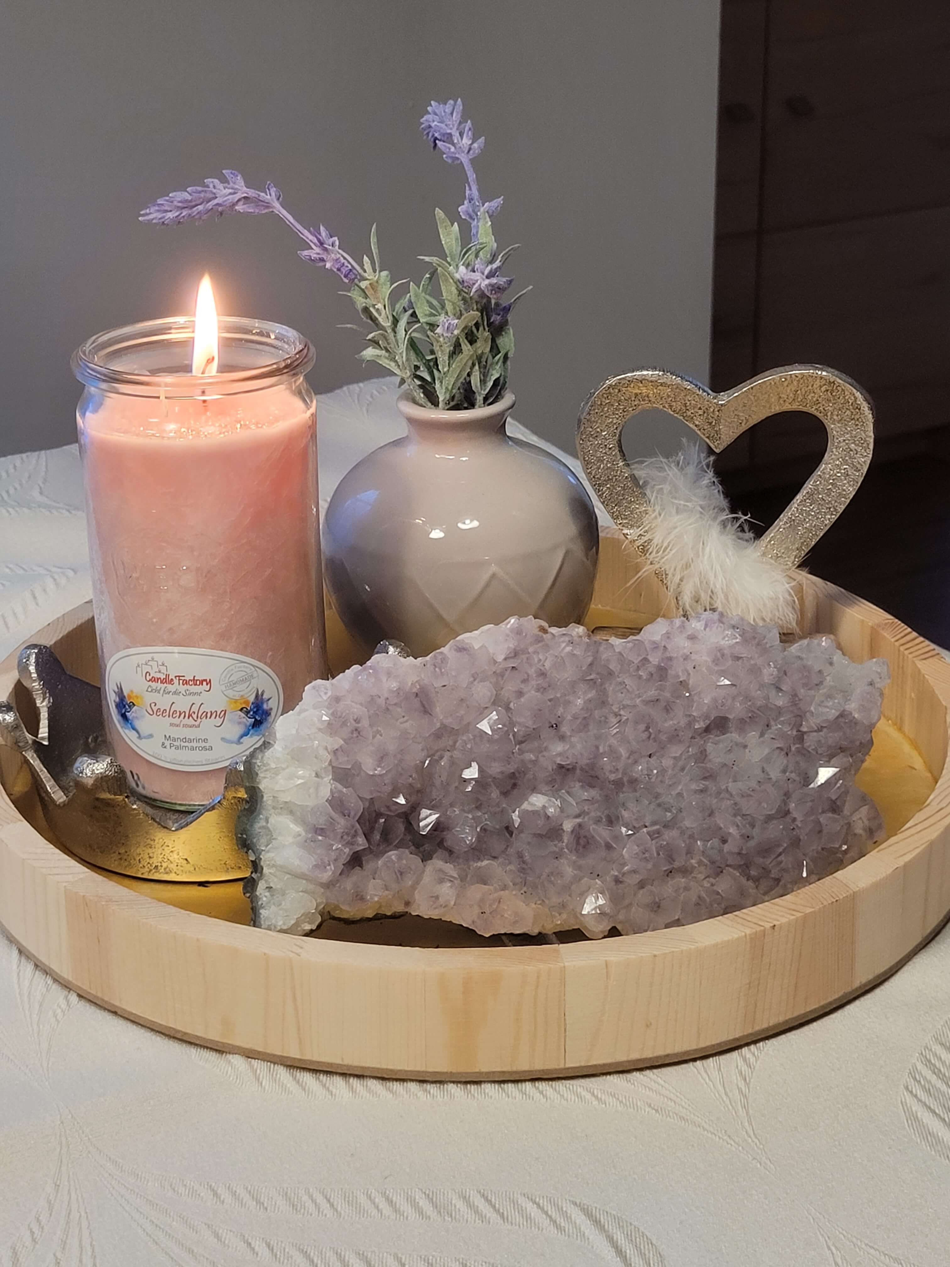 Brennende Kerze auf einem Holztablett mit einer Amethyst-Druse und einer Vase, in der Lavendelzweige stecken.