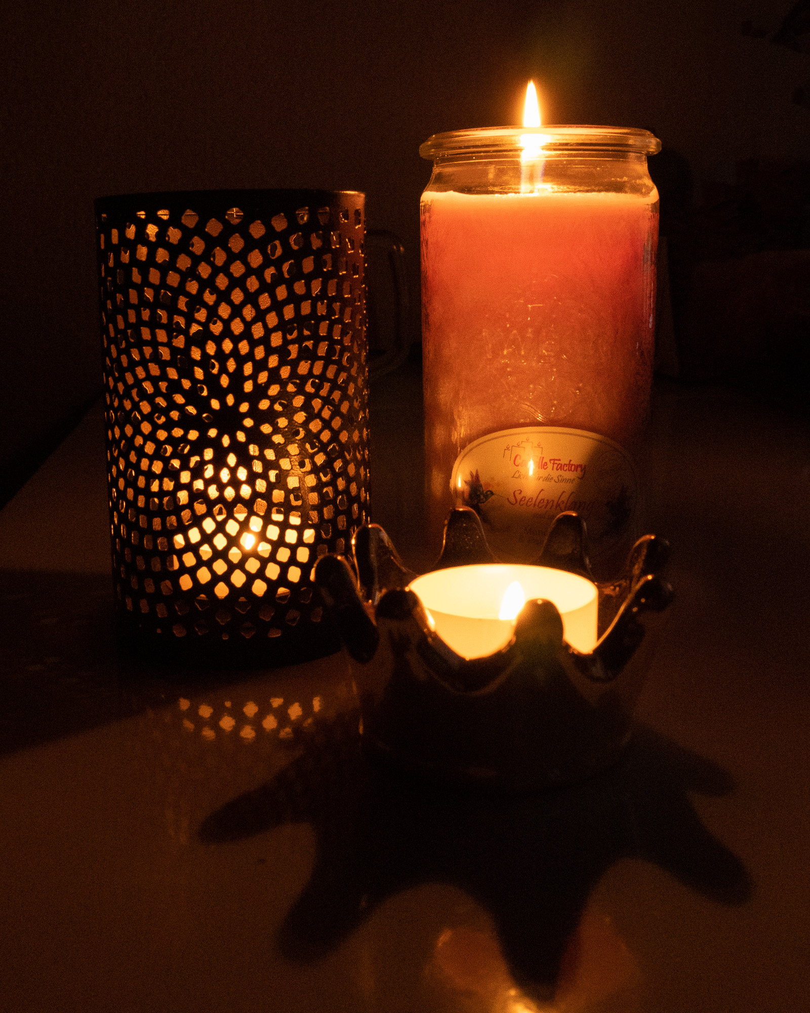 Brennende Kerze neben einem Teelichthalter mit Ornamenten