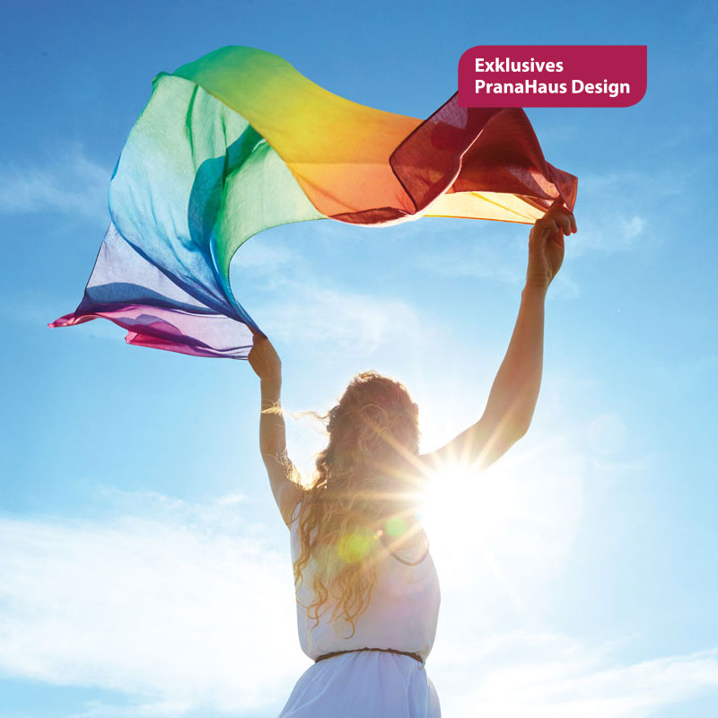 Frau schwingt einen Schal in Regenbogenfarben vor blauem Himmel. Die Sonne blitzt hinter ihr hervor.