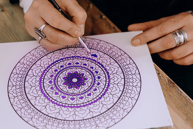Ein in violetten Tönen gehaltenenes Mandala auf weißem Papier.